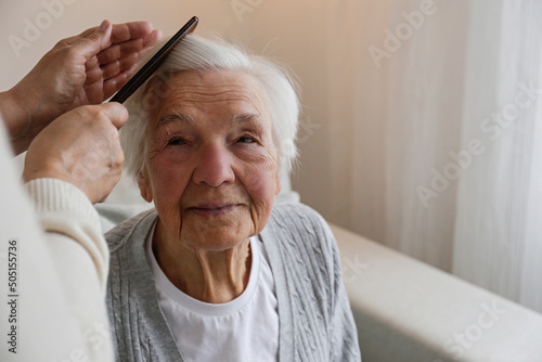Unrecognizable female expressing care towards an elderly lady, brushing her hair with a comb. Granddaughter helping granny with a haircut. Family values concept. lose up, copy space, background.