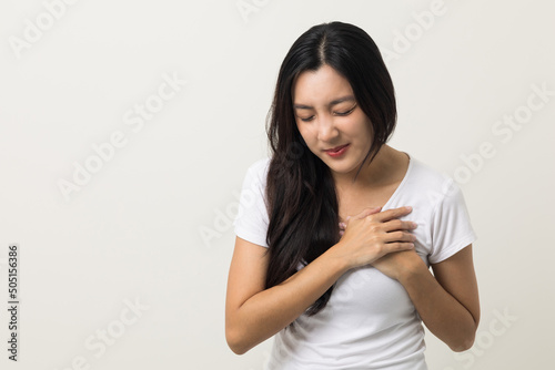 Asian woman around 25 year She felt a pain in her chest held her hand and squeezed it. She had a heart attack that needed treatment. Wearing white shirt standing on isolated background. © Chanakon