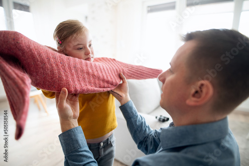 Valokuva Father helping his little daughter with Down syndrome to wear jumper at home