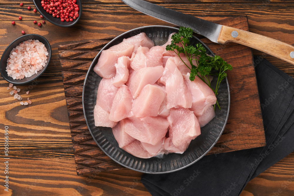 Raw chicken breast sliced or cut pieces on wooden cutting board with herbs and spices on old wooden table background. Raw chicken meat. Top view with copy space. Mock up.