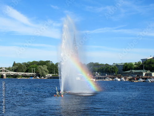 Fountain in a river creating a rainbow in front of a church in Pori, Finland.
