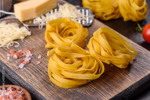 Raw tagliatelle paste with grated cheese, cherry tomatoes, spices and herbs on a wooden cutting board