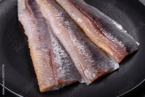 Delicious fresh herring fillet with salt, spices and herbs on a black plate