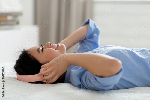 happy asian woman laying on bed, listening to music