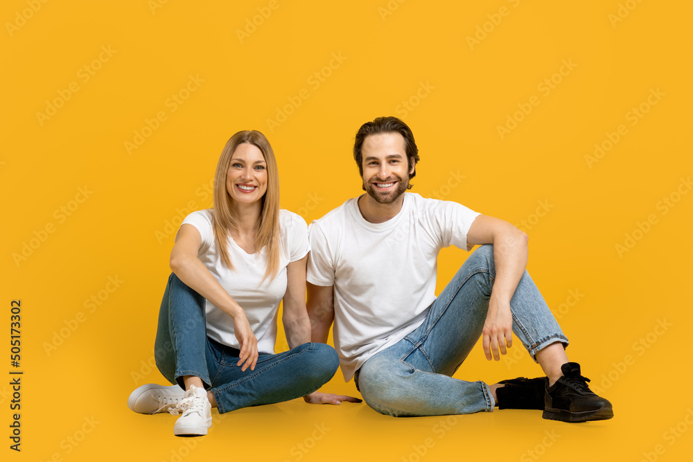 Happy confident handsome millennial european guy with beard and woman in white t-shorts sit on floor together Happy confident handsome millennial european guy with beard and woman in white t-shorts sit on floor together