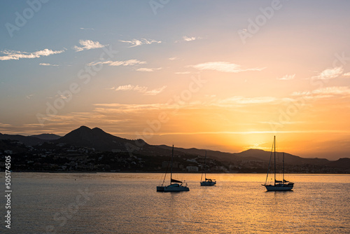 Summer sunrise, with mountain skyline and small sailing boats at anchor. Golden sunlight with light cirrus clouds. Costa del Sol, Malaga, Spain. © Victor Lucas