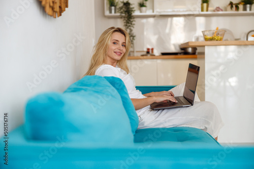 Foto Portrait of blonde beautiful female smiling to camera while working on laptop at home