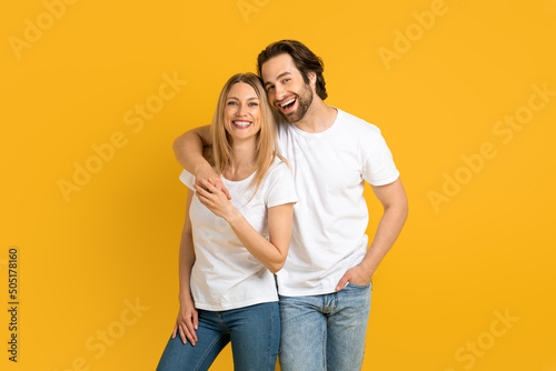 Glad young european guy and woman in white t-shirts hugging, have fun, isolated on yellow background