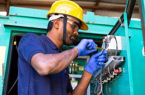 young electrical engineer with protective workware repairing or connecting wires by using screw driver at workplace - Concept of hard working, Skilled rapair man with safety precautions. photo
