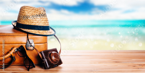 Fototapeta Naklejka Na Ścianę i Meble -  Vintage suitcase, sunglasses and hipster hat wooden deck and blur tropic sea background. Summer paradise cruise travel design layout banner. Tourism, beach, vacation travel destination concept mockup