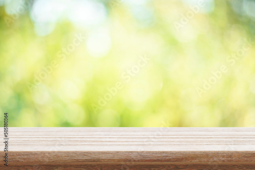 Empty wooden table and green bokeh nature background. Outdoor mockup for food product display montage. Summer garden blur backdrop and rustic desk placement.