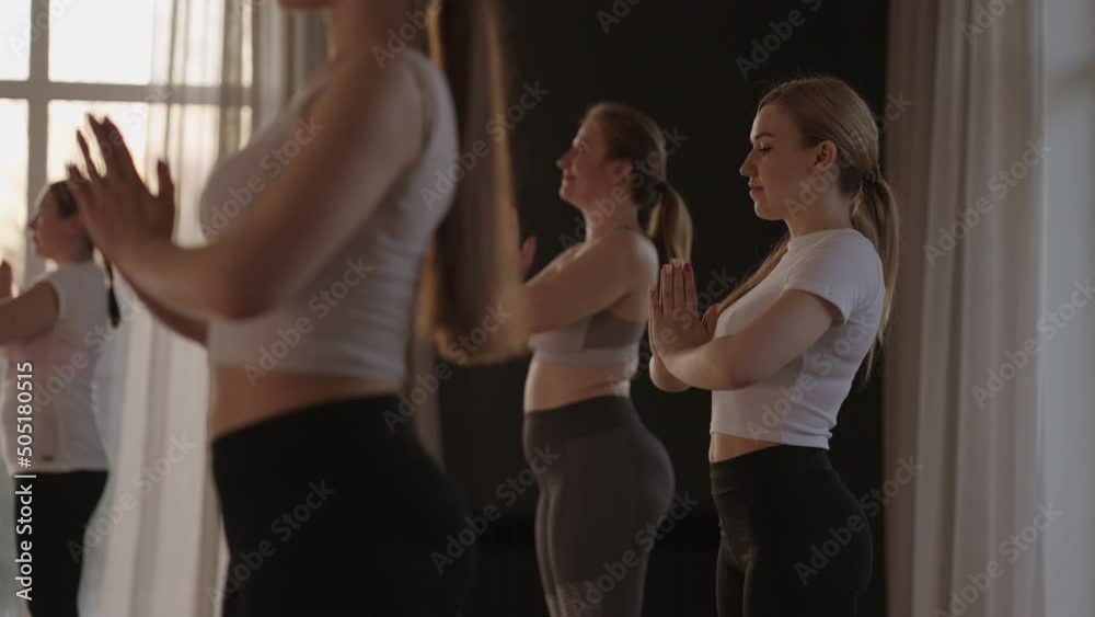 A group of women is engaged in stretching and balance with an instructor in a beautiful hall with large windows. Healthy lifestyle group classes. Women's sports club, slow motion A group of women is engaged in stretching and balance with an instructor in a beautiful hall with large windows. Healthy lifestyle group classes. Women's sports club, slow motion