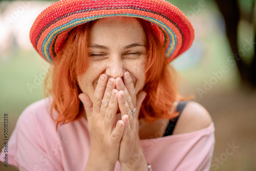 girl with red hair in a hat laughs and covers her face with her hands