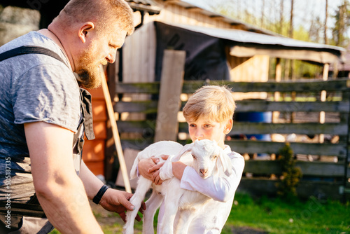 Preteen child boy holding the small goat. boy learn to work on the farm. Friendship of child and yeanling in countryside.