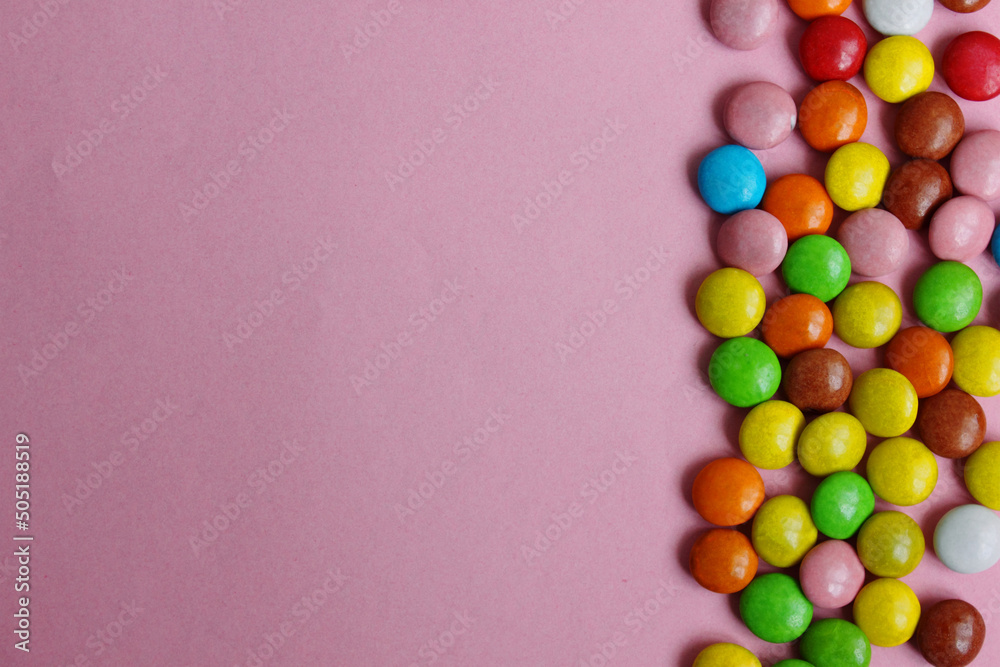 Obraz premium Lots of colorful candy and chewing gum. colorful candy on a pink background. Small candies in colored chocolate glaze. Located on the right. Chocolate snack. View from above. Copy space. Flat lay.