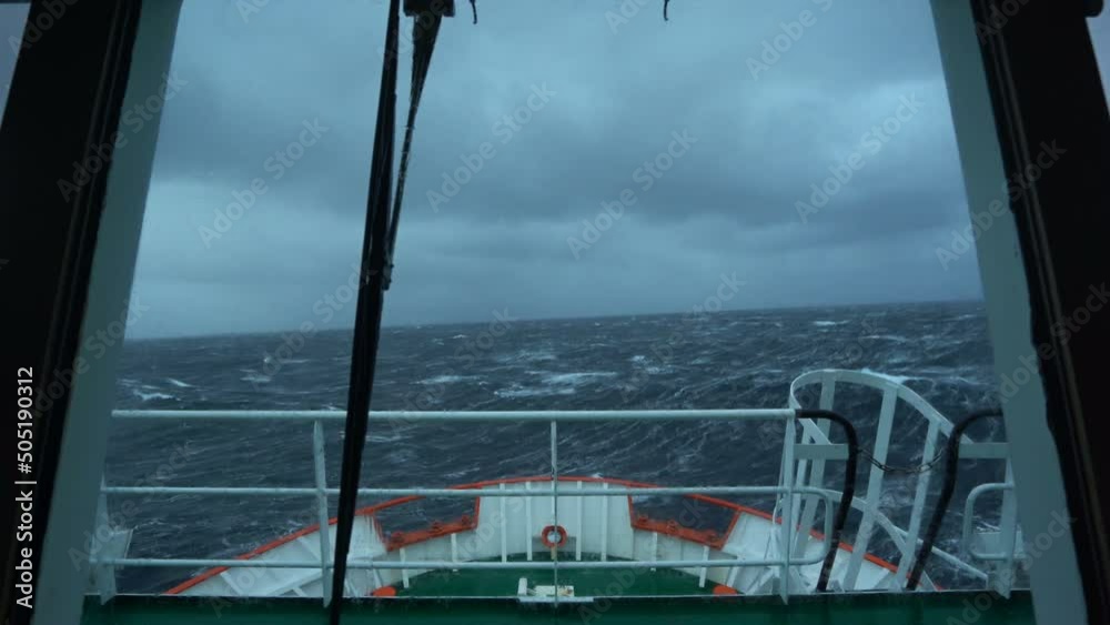 Vessel in storm. Bow breaks wave. Splashes of water. View from bridge. High waves. Strong pitching. White foam on water.