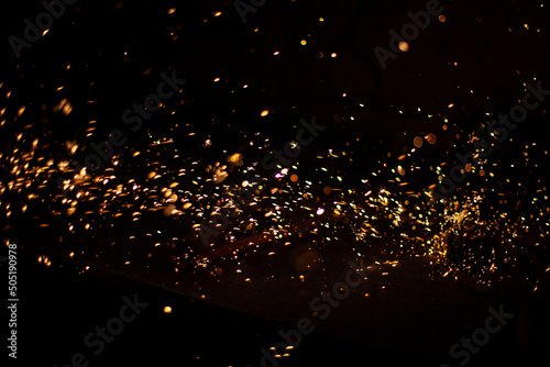 Sparks in dark. Flow of sparks from metal processing. Lights on black background. Work in workshop. Grinding steel. Many small particles burn brightly.