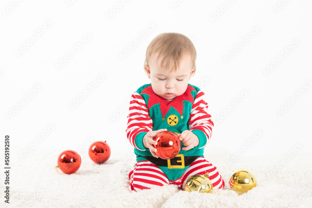 baby in elf costume grabbing christmas balls with serious expression baby in elf costume grabbing christmas balls with serious expression