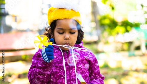 Close up shot of serious girl kid with winter wear on swing blowing soap bubble at park - concept of vacation, playful childhood and weekend activities. photo