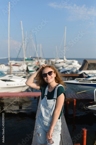 A smiling girl with sunglasses is on the pier waiting for the boat
