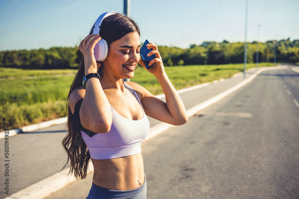 Portrait of a sporty young woman running outdoors. Shot of a fit young woman using a phone and earphones while exercising. Young woman listening to music while on a run.