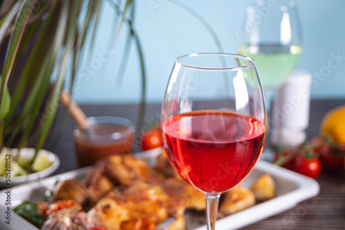 Glass of red wine and homemade food chicken tabaka with vegetables on the baking sheet on the background. Dinner concept.