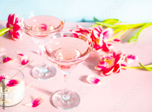 Glasses of pink cocktail with flowers and petals. Birthday party or Valentines day romatic couple date concept.