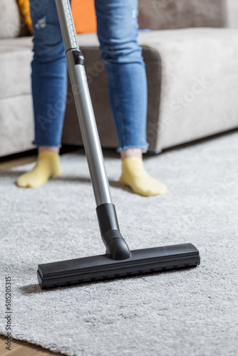 house cleaning concept. a close-up photo of a girl's legs and a vacuum cleaner brush. the girl cleans the house and vacuums the carpet.