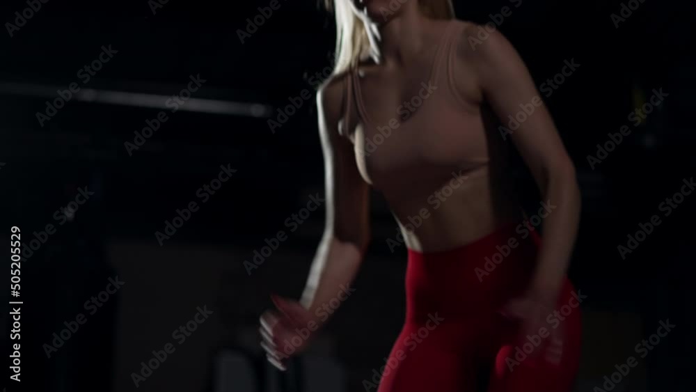 Unrecognizable slim sportswoman jumping on cube in slow motion in dark gym. Fit athletic Caucasian young woman working out indoors. Healthy lifestyle and motivation concept Unrecognizable slim sportswoman jumping on cube in slow motion in dark gym. Fit athletic Caucasian young woman working out indoors. Healthy lifestyle and motivation concept