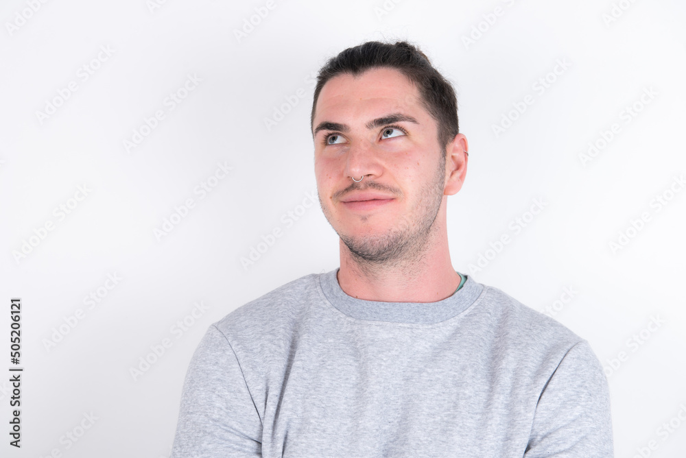 Young handsome dark haired man wearing fitted T-shirt over white wall looking aside into empty space thoughtful Young handsome dark haired man wearing fitted T-shirt over white wall looking aside into empty space thoughtful