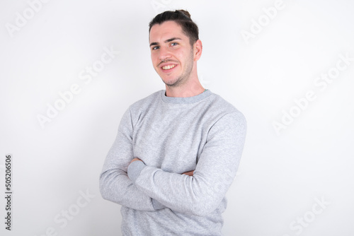 Young handsome dark haired man wearing fitted T-shirt over white wall  happy face smiling with crossed arms looking at the camera. Positive person. © Roquillo
