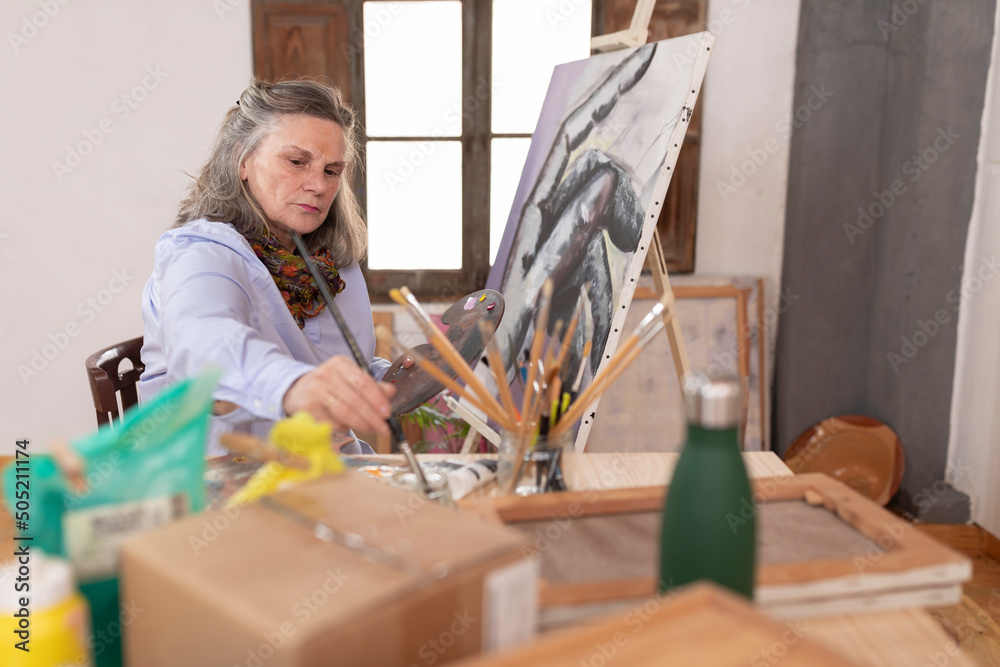 Mature artist woman cleaning the brush before using another color at her workshop Mature artist woman cleaning the brush before using another color at her workshop