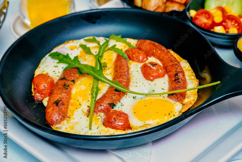 full irish breakfast with fried egg, sausages,  tomato in a cast iron pan.