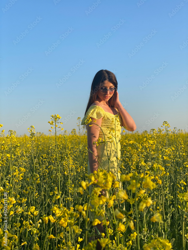 Happy woman turned away back, walks run along yellow field rapeseed, hands raised to side enjoys nature blue sky. Girl brunette long black hair fly in wind.