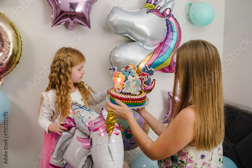 Happy birthday girl holding a cake. Decorated cake with toppers my little pony. Birthday party for 5 years. Balloons in the style of a multicolored unicorn, rainbow theme. Idea for decorating party.