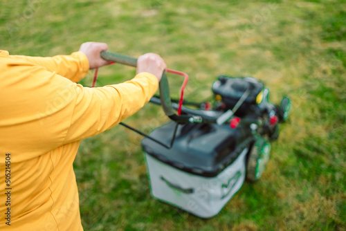 Worker mowing tall grass with electric or petrol lawn trimmer in city park or backyard.