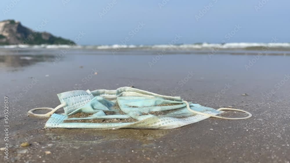 Discarded surgical face mask used disposable trash waste littering on sandy beach. Pandemic coronavirus ecological pollution problem. Close up shot editorial - day Discarded surgical face mask used disposable trash waste littering on sandy beach. Pandemic coronavirus ecological pollution problem. Close up shot editorial - day
