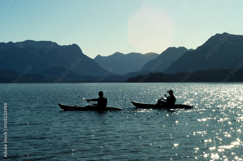 Blue silhouette of a mountain range with reflection of the sun in the waters of a lake people riding in kayaks. lifestyle concept Blue silhouette of a mountain range with reflection of the sun in the waters of a lake people riding in kayaks. lifestyle concept