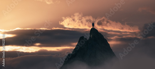 Adventurous Man Hiker Standing on top of a rocky mountain overlooking the dramatic landscape at sunset. 3d rendering peak. Background dramatic Cloudscape. Adventure Concept Artwork