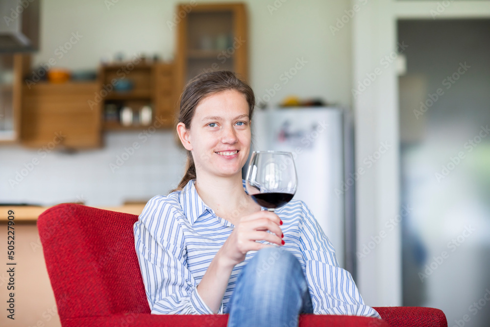 Junge blonde Frau zu Hause entspannt mit einem Glas Rotwein au fem Sofa ...