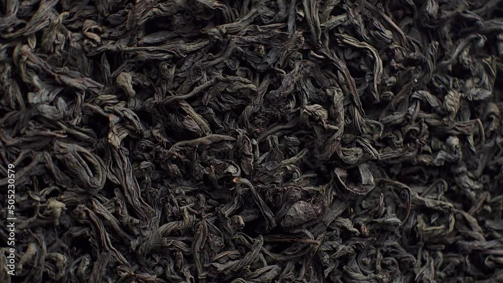 Background for a cafe or restaurant, black loose leaf tea sprinkled on a plate and spinning close up, tea advertising Background for a cafe or restaurant, black loose leaf tea sprinkled on a plate and spinning close up, tea advertising
