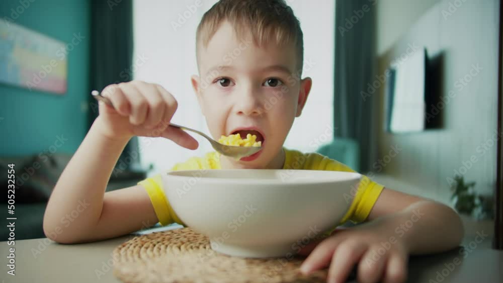 Portrait little hungry child cute boy sits at the dinner table, eats corn flakes with milk with an appetite of pleasure, enjoys breakfast. Portrait little hungry child cute boy sits at the dinner table, eats corn flakes with milk with an appetite of pleasure, enjoys breakfast.