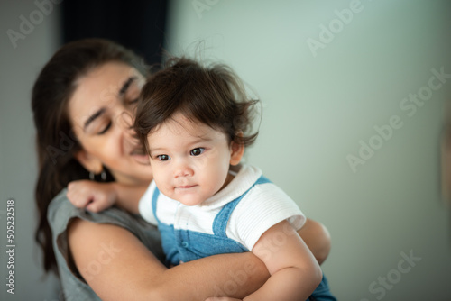 Cute little baby toddler pouncing and jumping while in the arms of young mother hugging at home