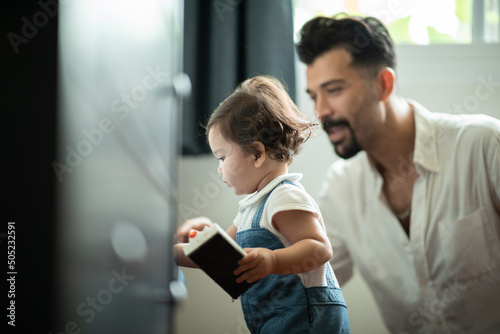 Cute little toddler baby boy playing and chewing marker pen with father while looking away and thinking at home