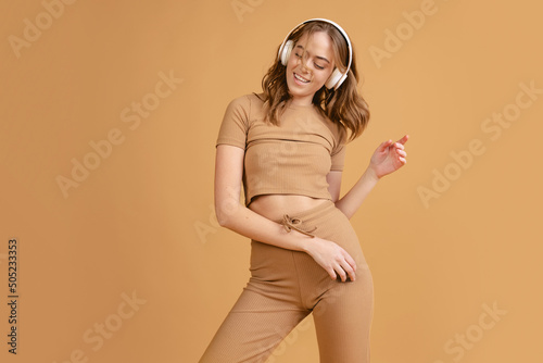 Happy girl, student listening to music and dancing isolated over brown color background. Concept of beauty, art, fashion, youth, monochrome