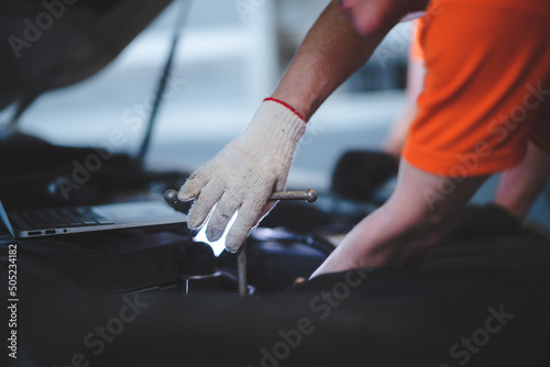 Smiling young car mechanic wearing uniform and hand gloves pushing and checking new tires in stock in garage for customer and maintaining inventory