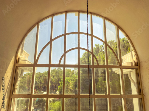 window to the floor in a hotel for tourists. glass window with a metal grill on top. greenery  trees outside
