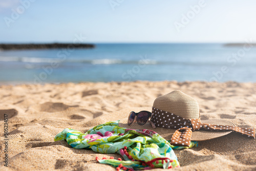 Hat, sunglasses and a green sarong on the sand of a sunny beach