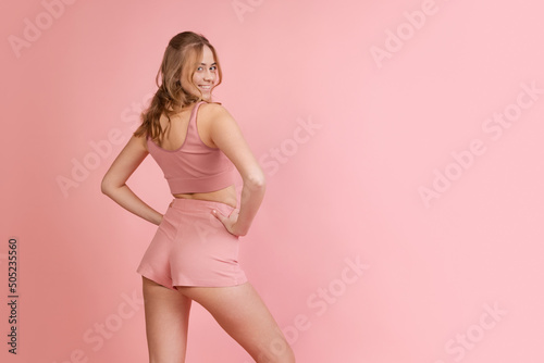 Monochrome portrait of young attractive woman in shorts and crop top isolated on pink background. Concept of beauty, art, fashion, youth, monochrome