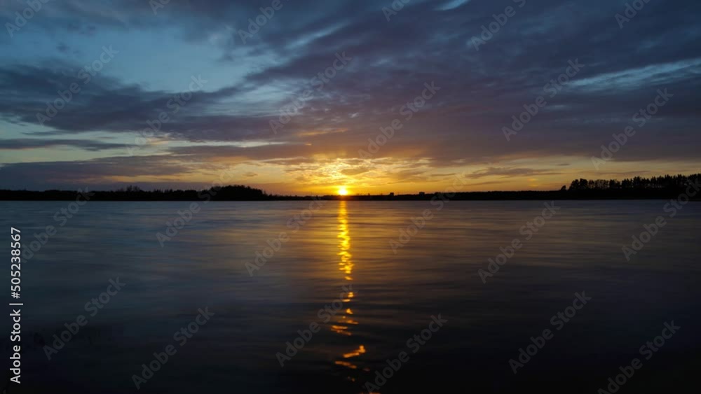 Time lapse colorful summer beach sunset with beautiful orange blue cloudy sky moving over lake with reflection on water Time lapse colorful summer beach sunset with beautiful orange blue cloudy sky moving over lake with reflection on water